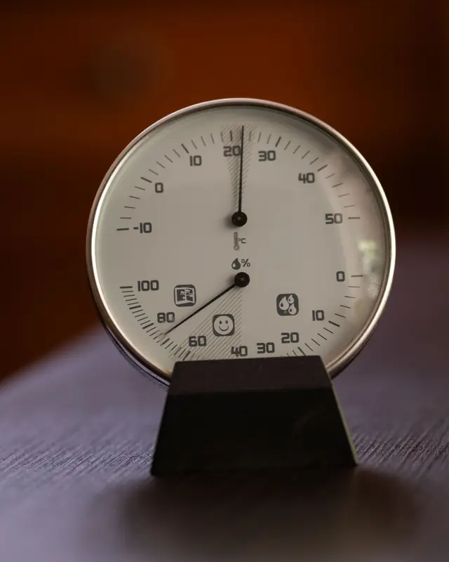 A round analog hygrometer and thermometer on a wooden table, with one dial for temperature and one for relative humidity