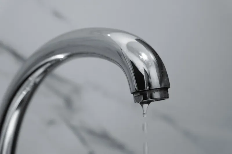 A chrome bathroom faucet with a drop of water falling from its spout