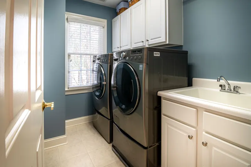 A home laundry room with a front-load washer and dryer on pedestals, a utility sink and white cabinets