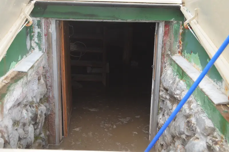 Muddy floodwater standing at the bottom of a stone-walled basement entrance, with wooden stairs and shelving inside