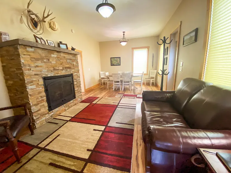 A living room with a gas fireplace insert set into a stacked-stone surround with a wood mantel, a leather sofa and a dining table beyond