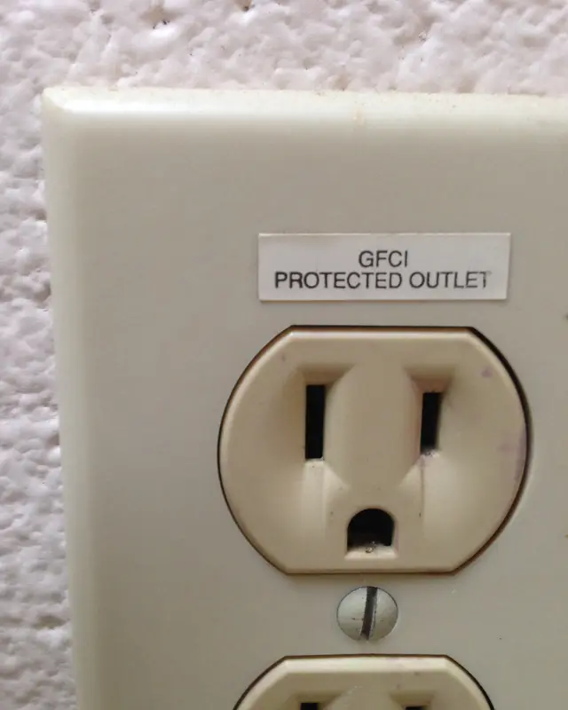 A beige duplex wall outlet with a printed label reading GFCI protected outlet