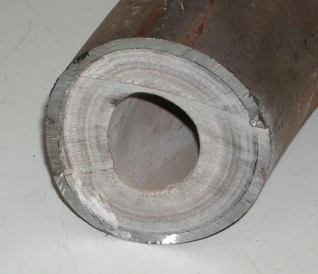 The cut end of a steel pipe with a thick white crust of mineral scale lining the inside wall