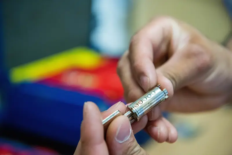 Close-up of a locksmith's hands holding a lock cylinder and fitting a small pin into it while rekeying the lock