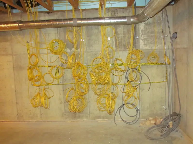 Coils of new yellow electrical cable hanging along a concrete wall before being connected to breaker panels