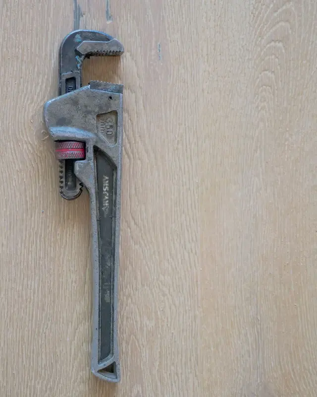 A steel pipe wrench lying on a light wooden surface