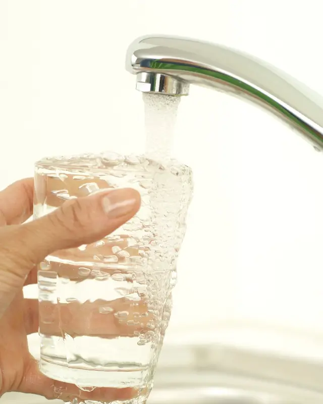 A hand holding a glass under a chrome kitchen faucet as tap water fills it