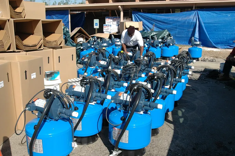 Rows of new well pumps mounted on small blue tanks, lined up outdoors next to their shipping boxes