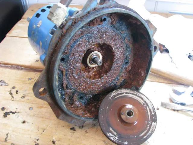 A disassembled well pump with its impeller removed, both covered in heavy rust-colored mineral deposits