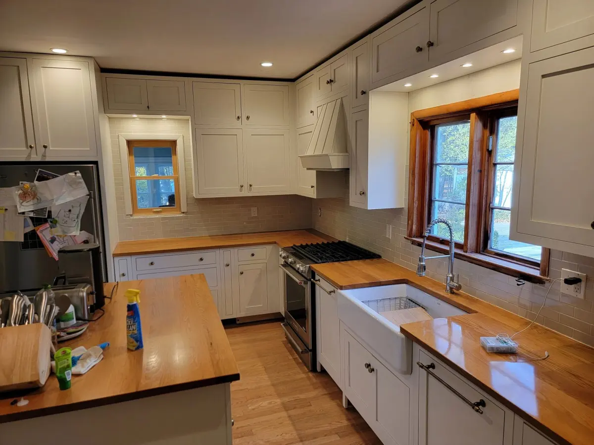 Finished kitchen with white shaker cabinets, butcher-block counters, a farmhouse sink and a range hood